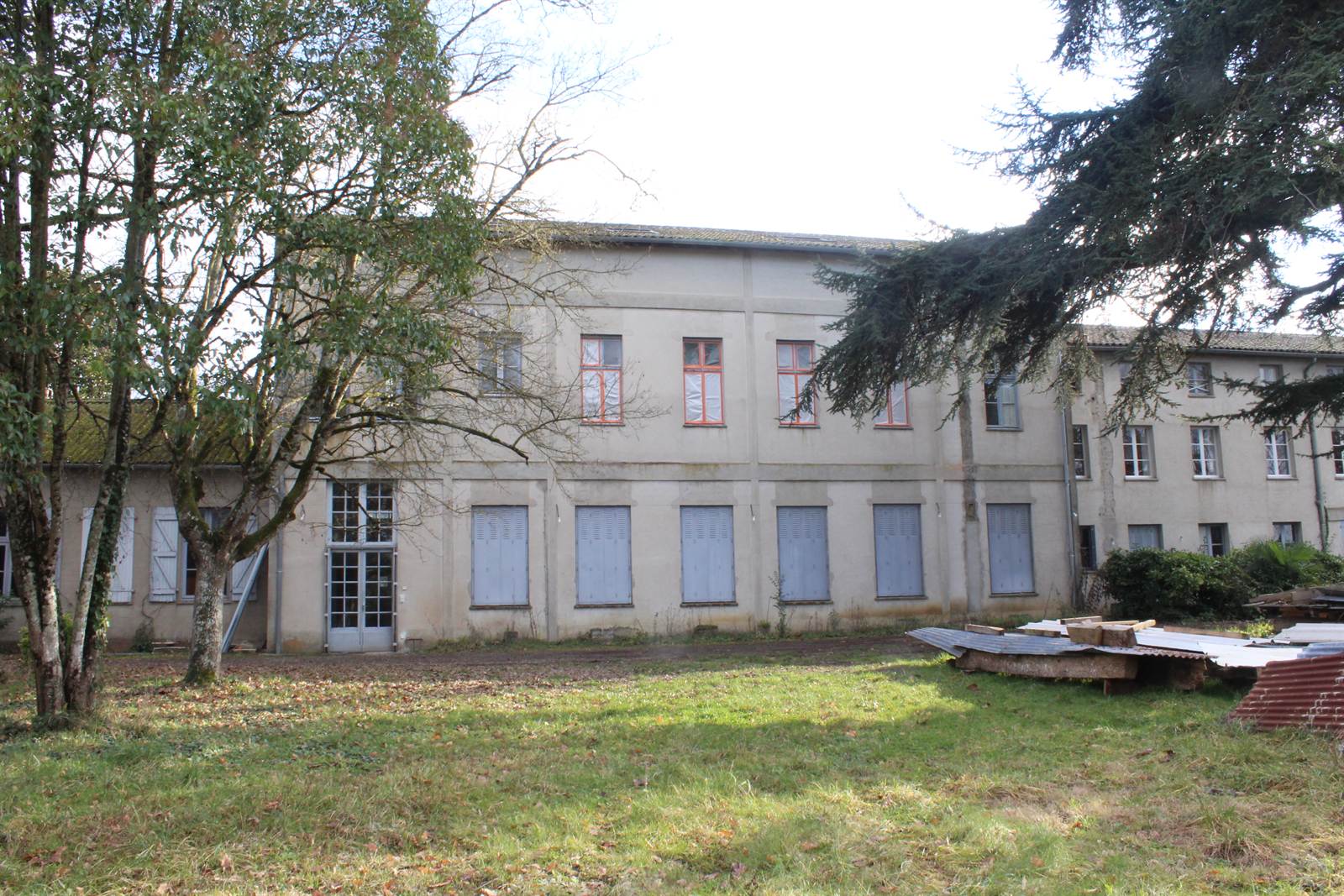 The long range seen across the meadow, trees in front of a two-storey rendered facade.