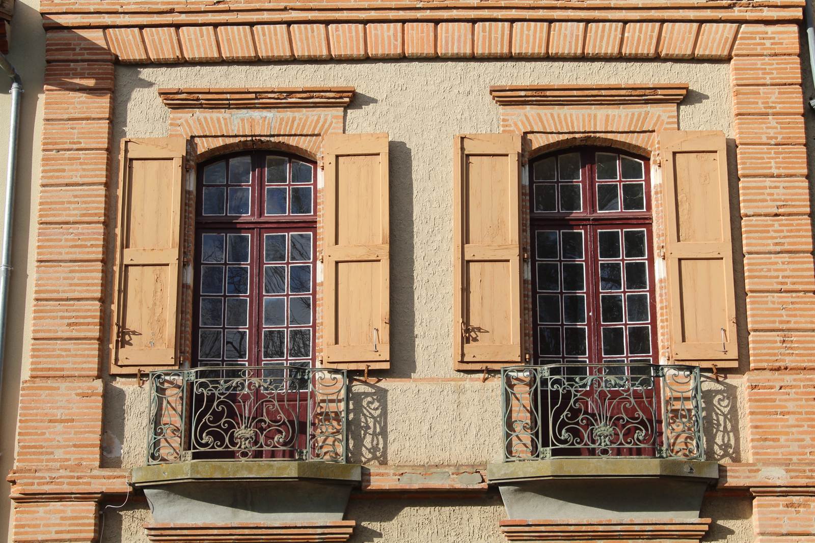 Two tall windows in moulded brick surrounds, with timber shutters and wrought-iron balconies.