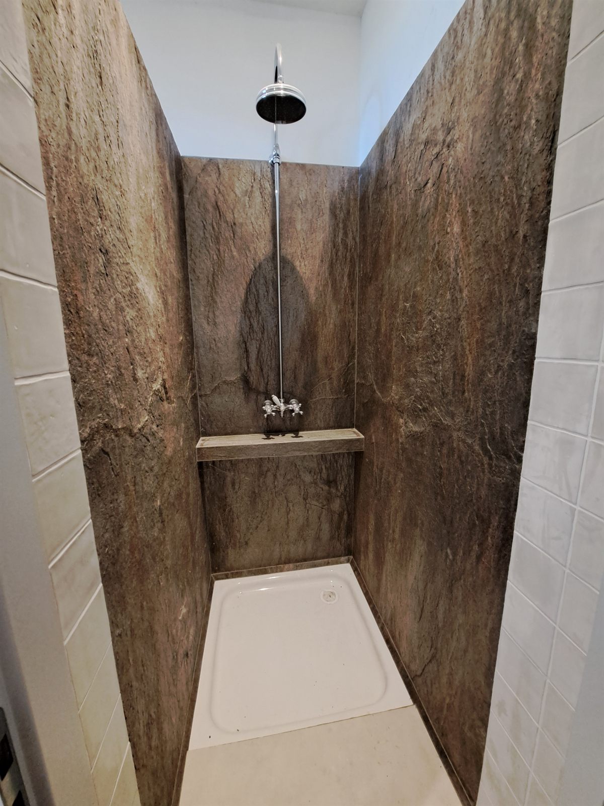 Une cabine de douche finie en panneaux effet pierre, avec pomme de pluie, mitigeur et receveur.