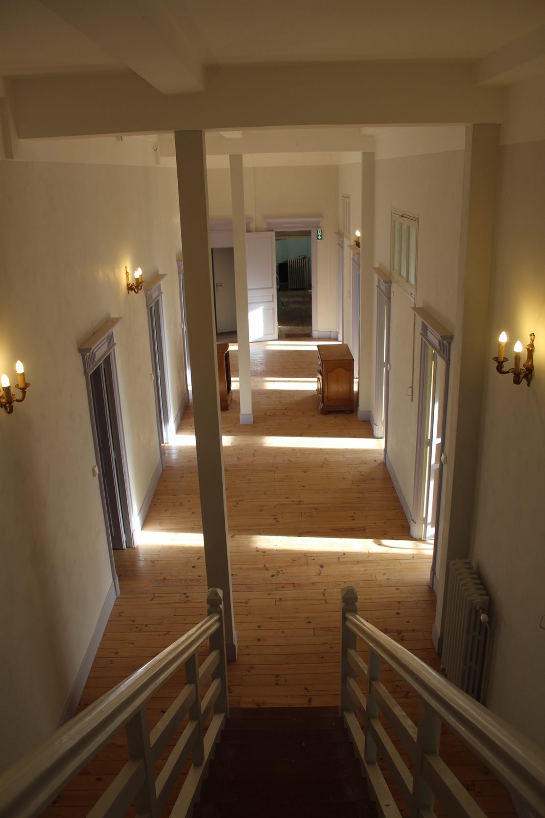 Un couloir vu depuis le haut de l’escalier, avec une rampe peinte et un plancher de bois.