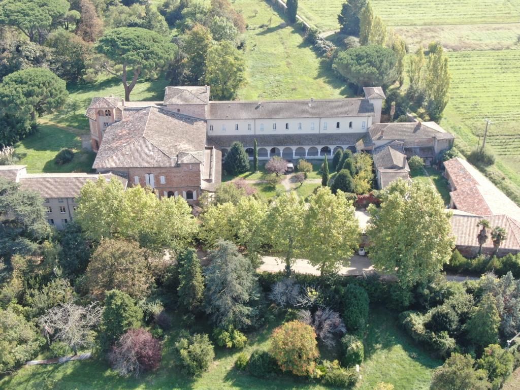 The estate from the air: the cloister range around its garden, farm buildings, and cultivated land beyond.